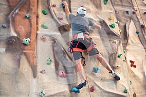 Young man practicing rock climbing on artificial wall indoors.