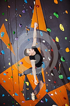 Young man practicing rock-climbing in climbing gym