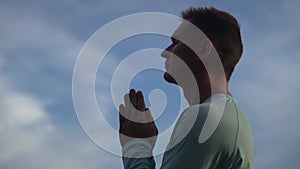 Young Man pray on blue sky background. Repentance, regret and hope concept