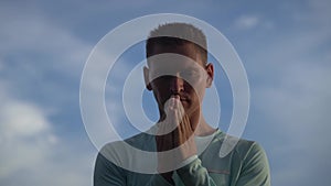 Young Man pray on blue sky background. Repentance, regret and hope concept