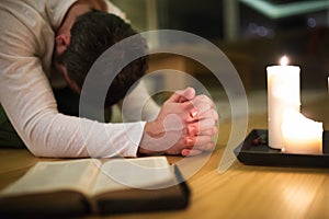 Young man praying, kneeling, Bible and candle next to him.