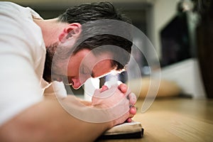 Young man praying, kneeling on the floor, hands on Bible