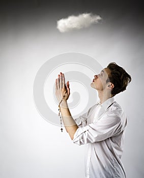 Young man is praying with rosary beads. Young man with rosary and cloud is overhead