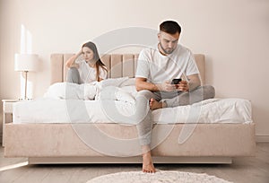 Young man preferring smartphone over girlfriend on bed at home. Relationship problems