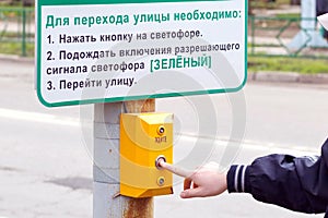 The young man presses the traffic light button to go to the opposite side of the street.