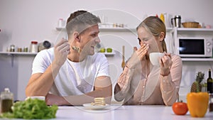 Young man pretending to feed girl with cake, couple having fun in kitchen, flirt