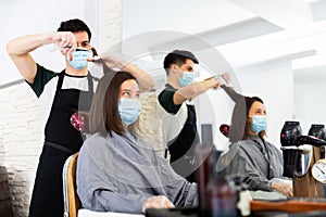 Young man professional hairdresser in mask cut female`s hair