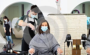 Young man professional hairdresser in mask cut female`s hair