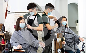 Young man professional hairdresser in mask cut female's hair