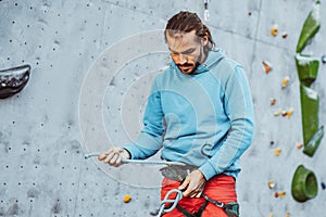 Young man professional rock climber checking sports equipment before climbing at training center in sunny day, outdoors