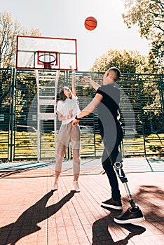 Young man with prosthetic leg playing basketball with his friend at a court