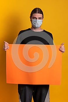 Young man with protective mask against virus epidemy is holding an empty orange cardboard.