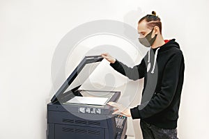 Young man in a protective mask makes copies of documents on a copy machine