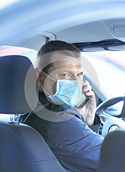 A young man in a protective mask is sitting in a right-hand drive car and calls on his mobile phone. Taxi driver. Coronavirus