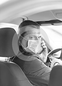 A young man in a protective mask is sitting in a right-hand drive car and calls on his mobile phone. Taxi driver. Coronavirus