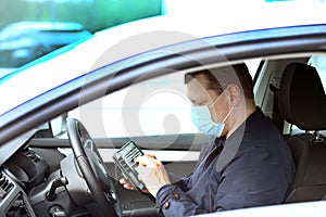 A young man in a protective mask is sitting in a right-hand drive car and calls on his mobile phone. Taxi driver. Coronavirus