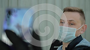 Young man in a protective mask using mobile phone for video conference on street