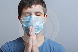 Young man in a protective medical mask folded hands near chin and praying to God, doctor on studio backgroung, concept life and