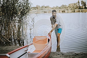 Young man pulling canoe into calm lake