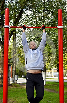 Young man pulls up on the bar during workout, outdoor sports