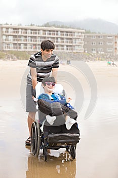 Young man pushing disabled little boy in wheelchair on beach