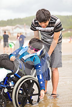 Young man pushing disabled little boy in wheelchair on beach