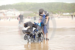 Young man pushing disabled little boy in wheelchair on beach