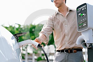 Young man put EV charger to recharge electric car battery. Expedient