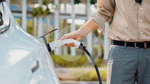 Young man put EV charger to recharge electric car battery. Expedient