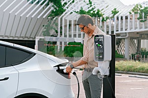 Young man put EV charger to recharge electric car battery. Expedient