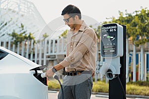 Young man put EV charger to recharge electric car battery. Expedient