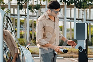 Young man put EV charger to recharge electric car battery. Expedient