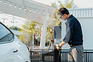 Young man put EV charger to recharge electric car battery. Expedient