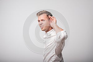 A young man puts a hand on the ear try to hear the whisper, isolated on a white background.