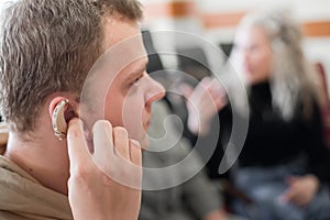 A young man puts on a hearing aid. Portable sound amplifier for the deaf and hearing impaired
