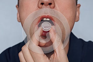 Young man puts in his mouth a sucking pill for sore throat. Self-medication for flu and cold. Sick with a sore throat, mint for fr