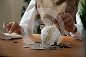 Young man putting coin into piggy bank.