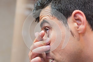Young man putting contact lens in his eye