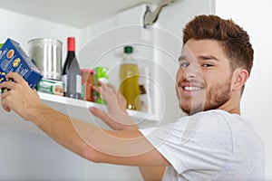 Young man putting food away in cupboard