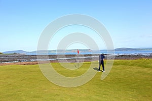 A young man putting on a golf green surrounded by the beautiful views of the sea outside Inverness, Scotland