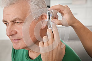 Young man putting hearing aid in father`s ear, closeup