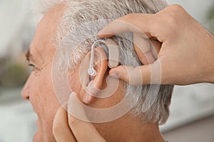 Young man putting hearing aid in father`s ear indoors