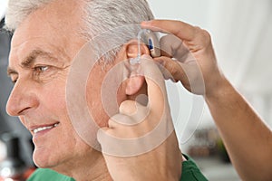 Young man putting hearing aid in father`s ear indoors