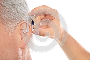 Young man putting hearing aid in father`s ear on white background