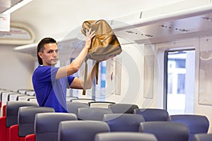 Young man putting luggage into overhead locker at
