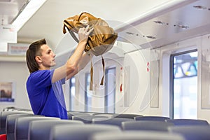 Young man putting luggage into overhead locker at train