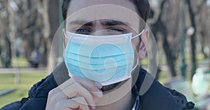 Young man putting on medical protective mask outdoors