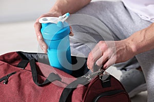 Young man putting shaker with protein into bag on blurred background, closeup