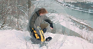 young man putting things to backback while hicking in the mountains in winter