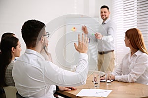 Young man raising hand to ask question at business training in room